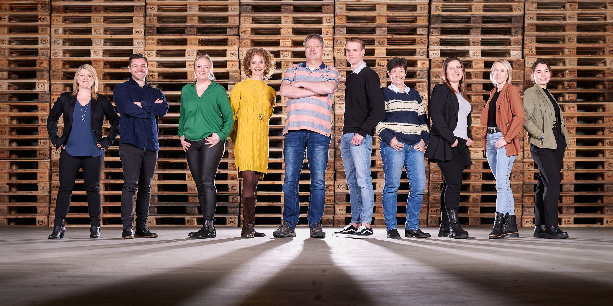 gruppenbild-team-vor-paletten-wand-in-halle
