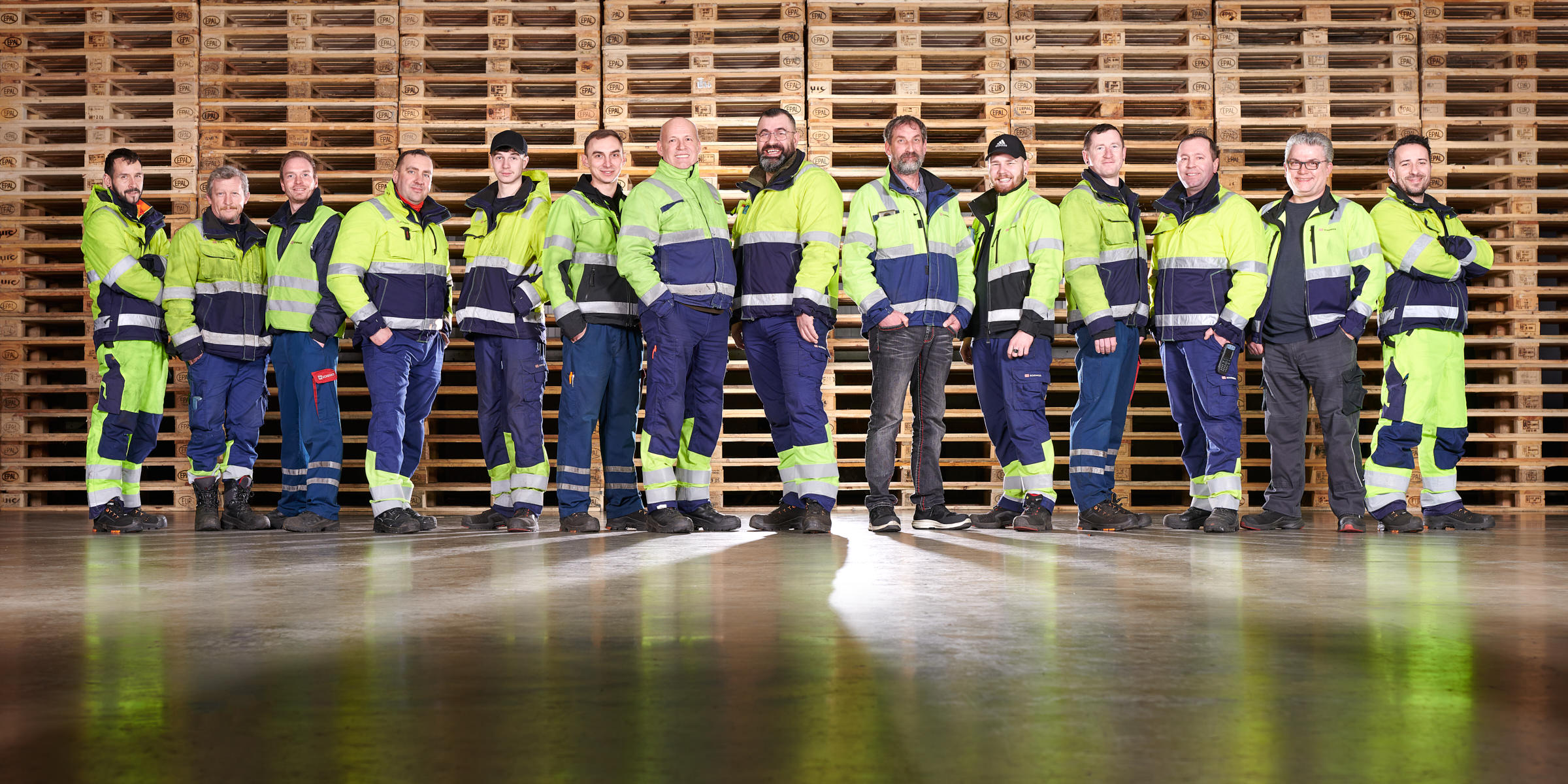 gruppenbild-team-logistik-arbeiter-vor-palletten-wand
